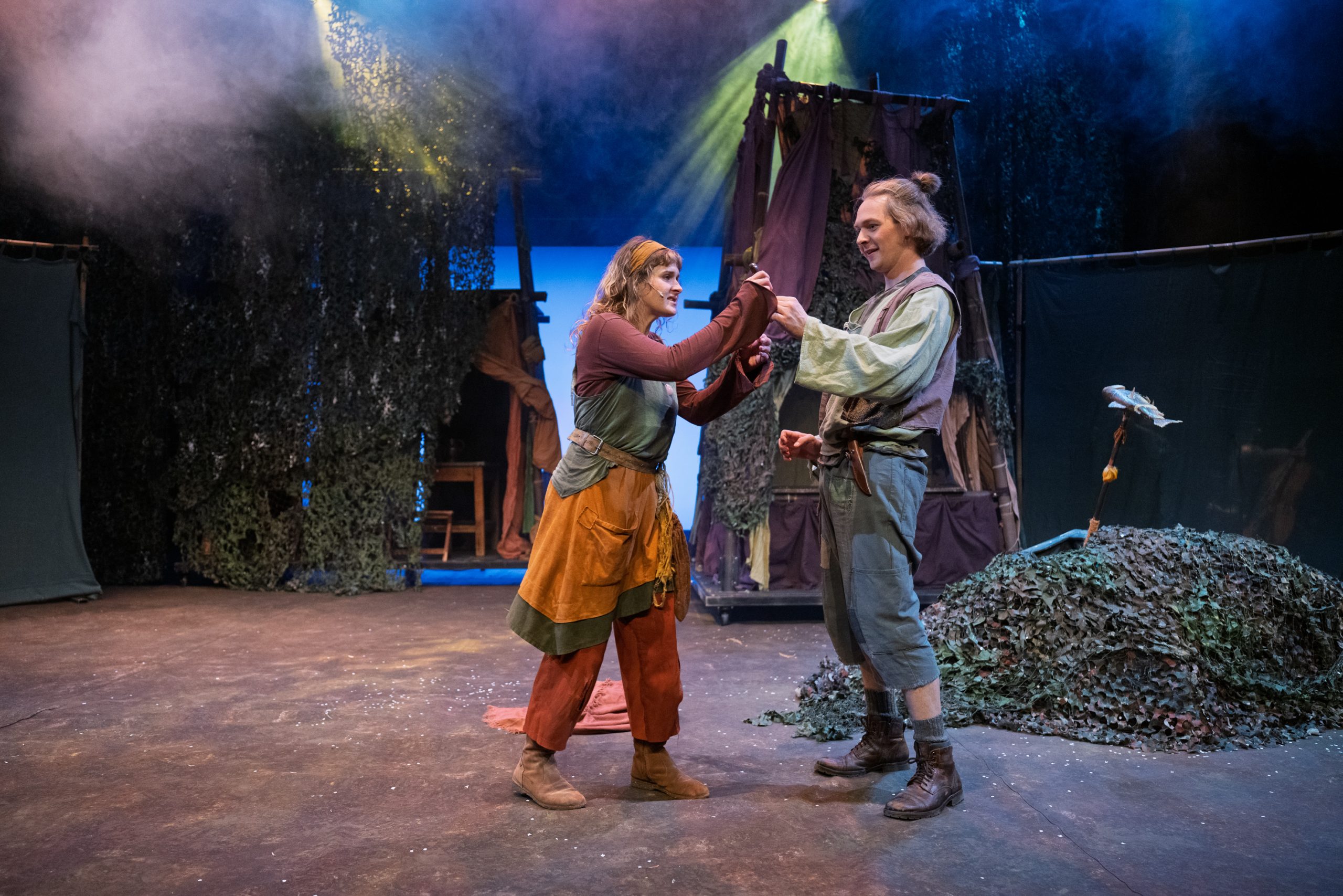 Zwei Schauspieler in mittelalterlicher Kleidung stehen auf einer Bühne und berühren sich mit den Fäusten.