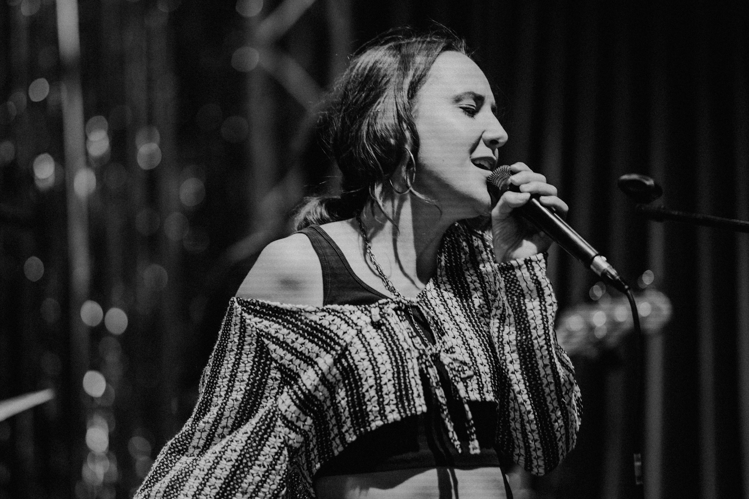 Sängerin mit offenem kariertem Hemd über schwarzem Top hält Mikrofon auf einer Bühne