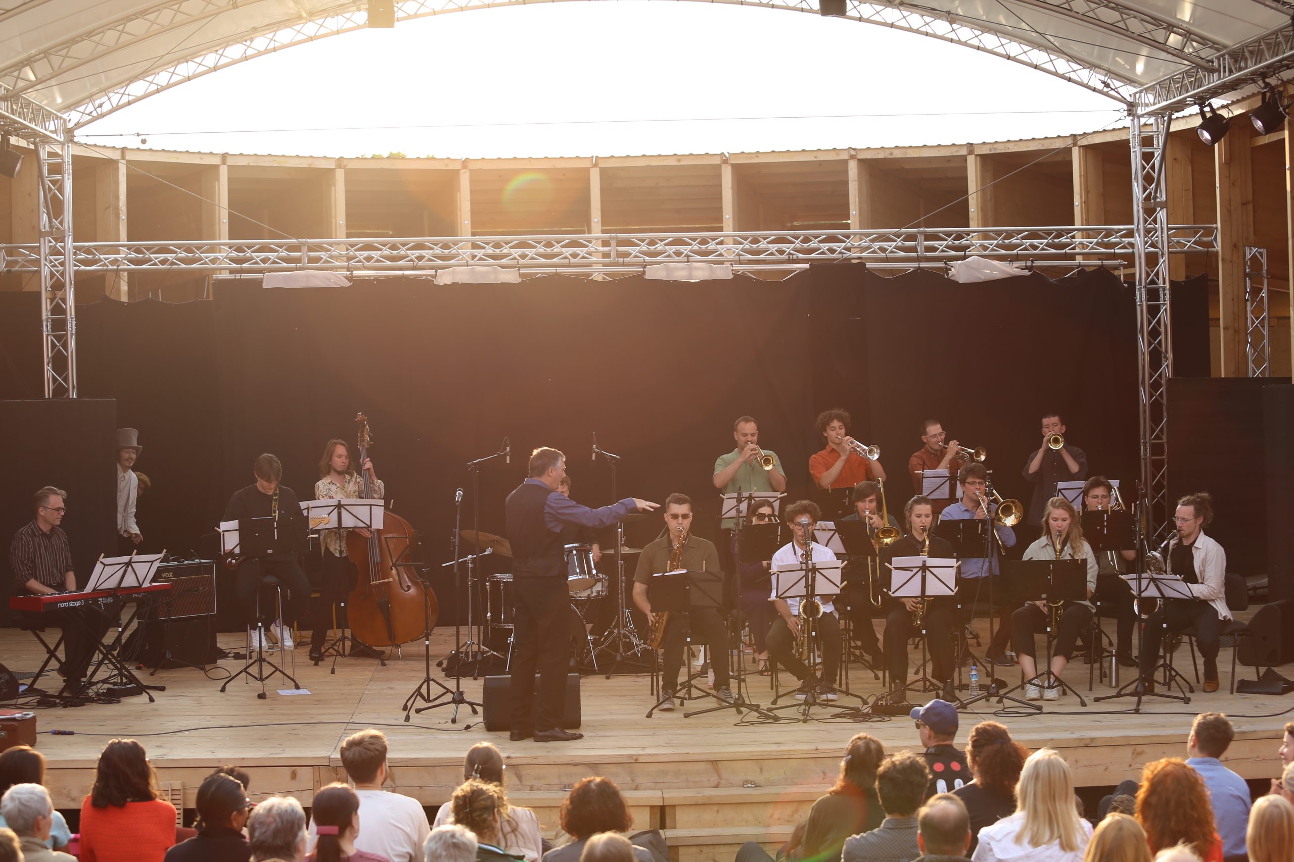 Big Band musiziert vor Publikum auf einer hölzernen Open-Air-Bühne.