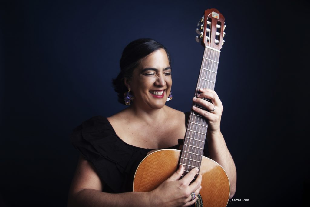 Eine Frau hält lächelnd eine Gitarre in den Händen.