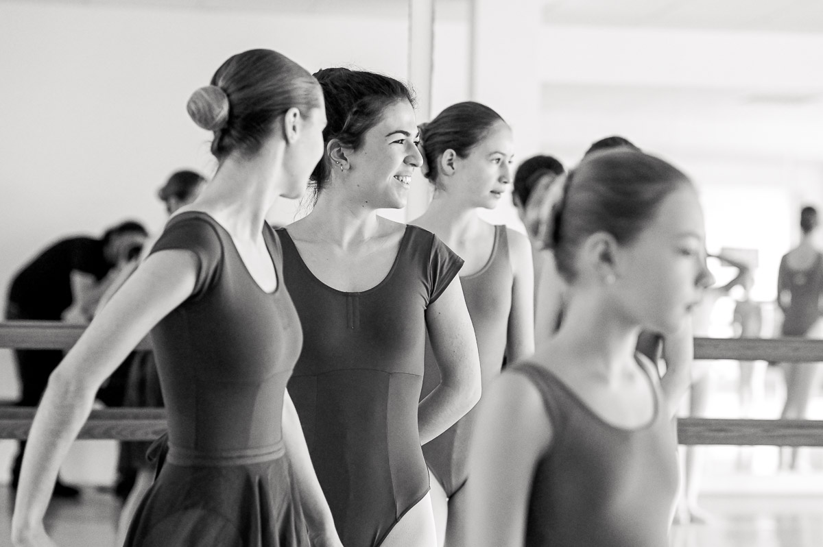 Mehrere Balletttänzerinnen in enger Tanzkleidung stehen nebeneinander vor einer Ballettstange in einem Tanzstudio