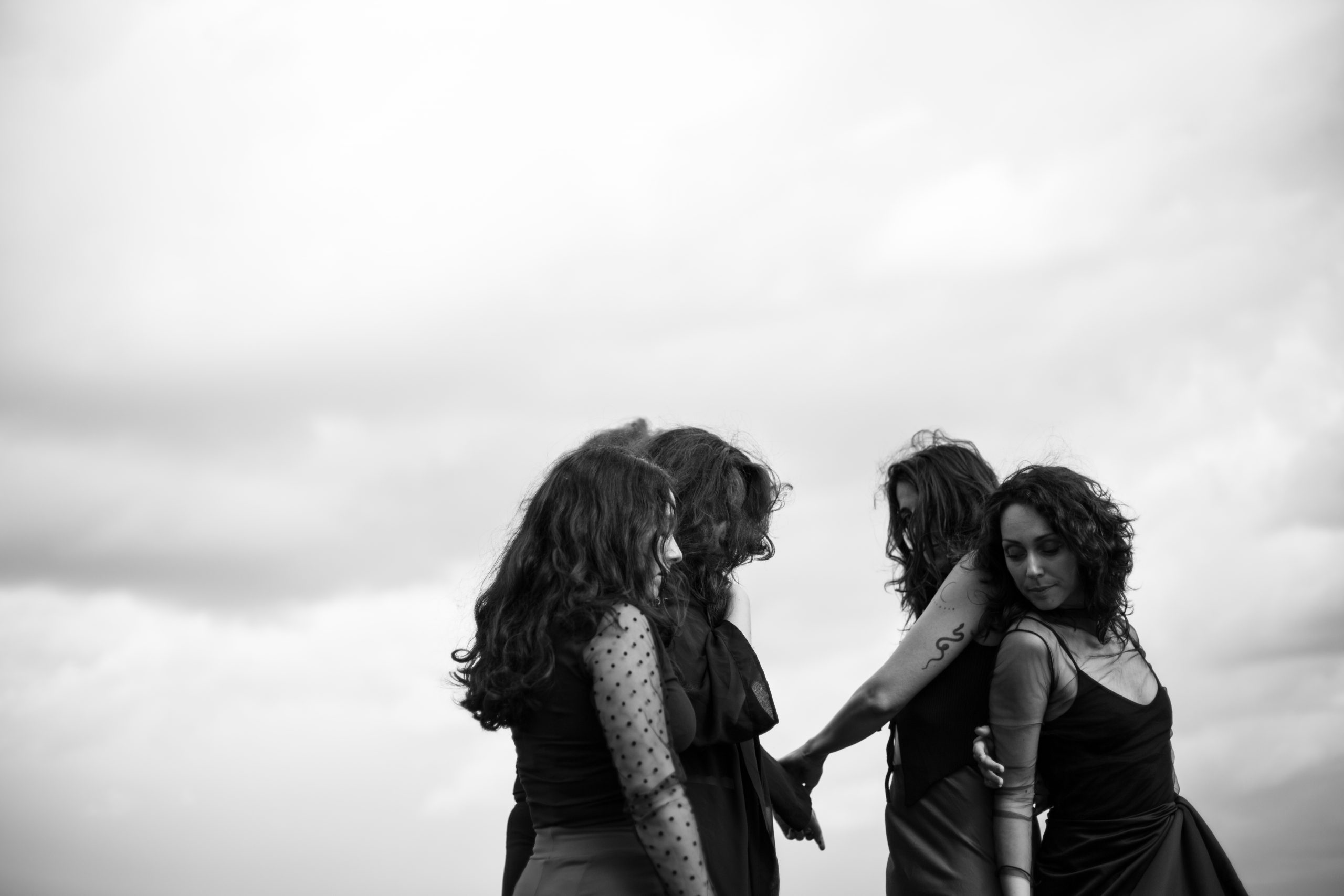 Ein Gruppe von Frauen in schwarzen Kleidern stehn vor einem grauen Himmel.